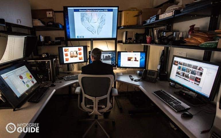 information systems management officer in front of several monitors