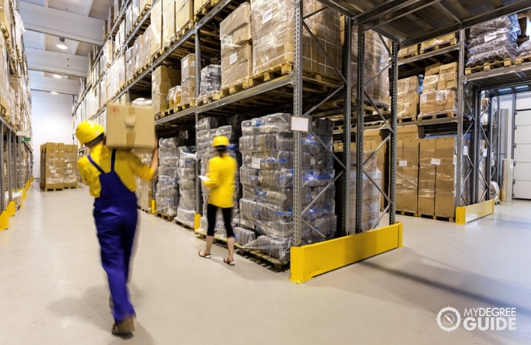 warehouse worker moving a box while being supervised by manager